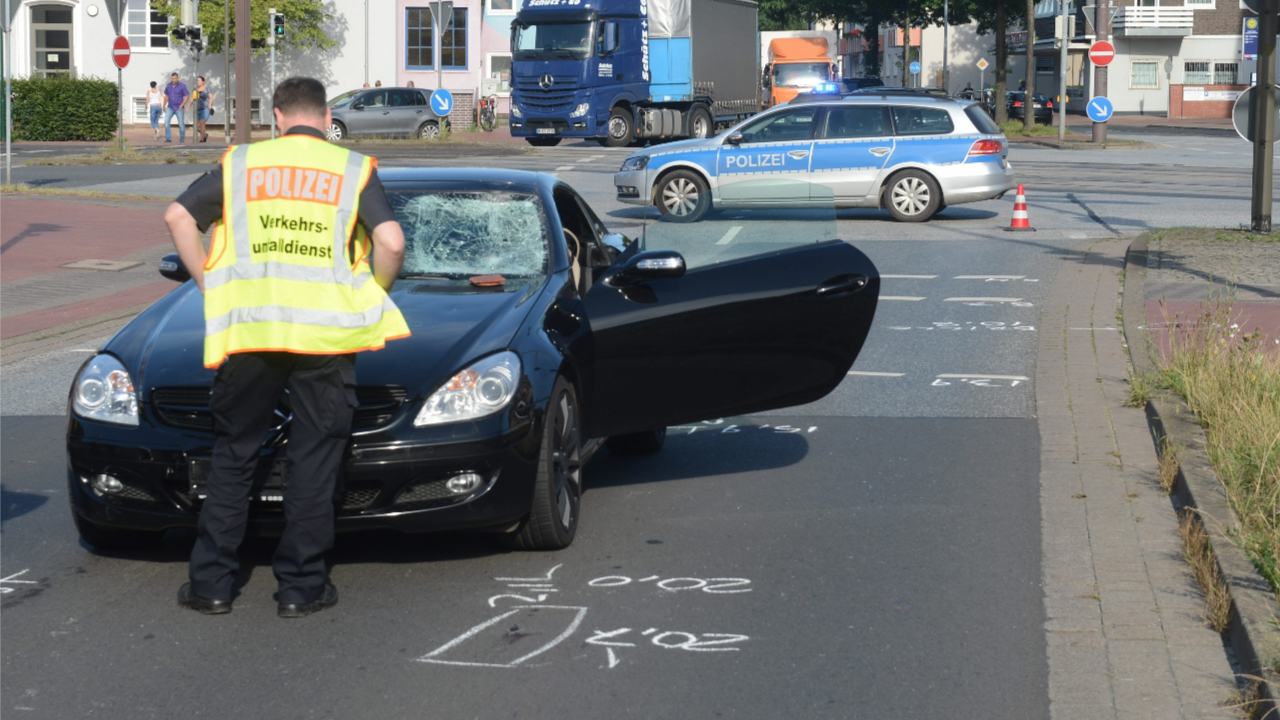 Ein Polizist steht vor dem Unfallwagen. Die Frontscheibe ist von dem Aufprall kaputt
